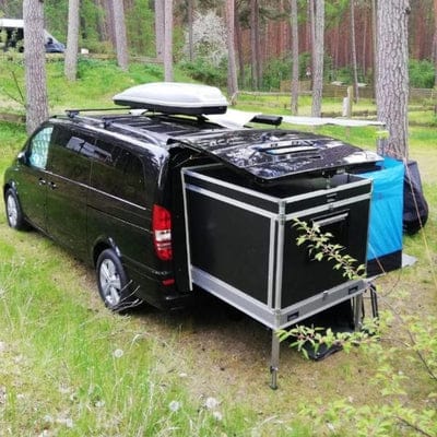 Schwarzer Van mit ausgezogenem Schlafmodul und Dachbox auf einem Waldstellplatz
